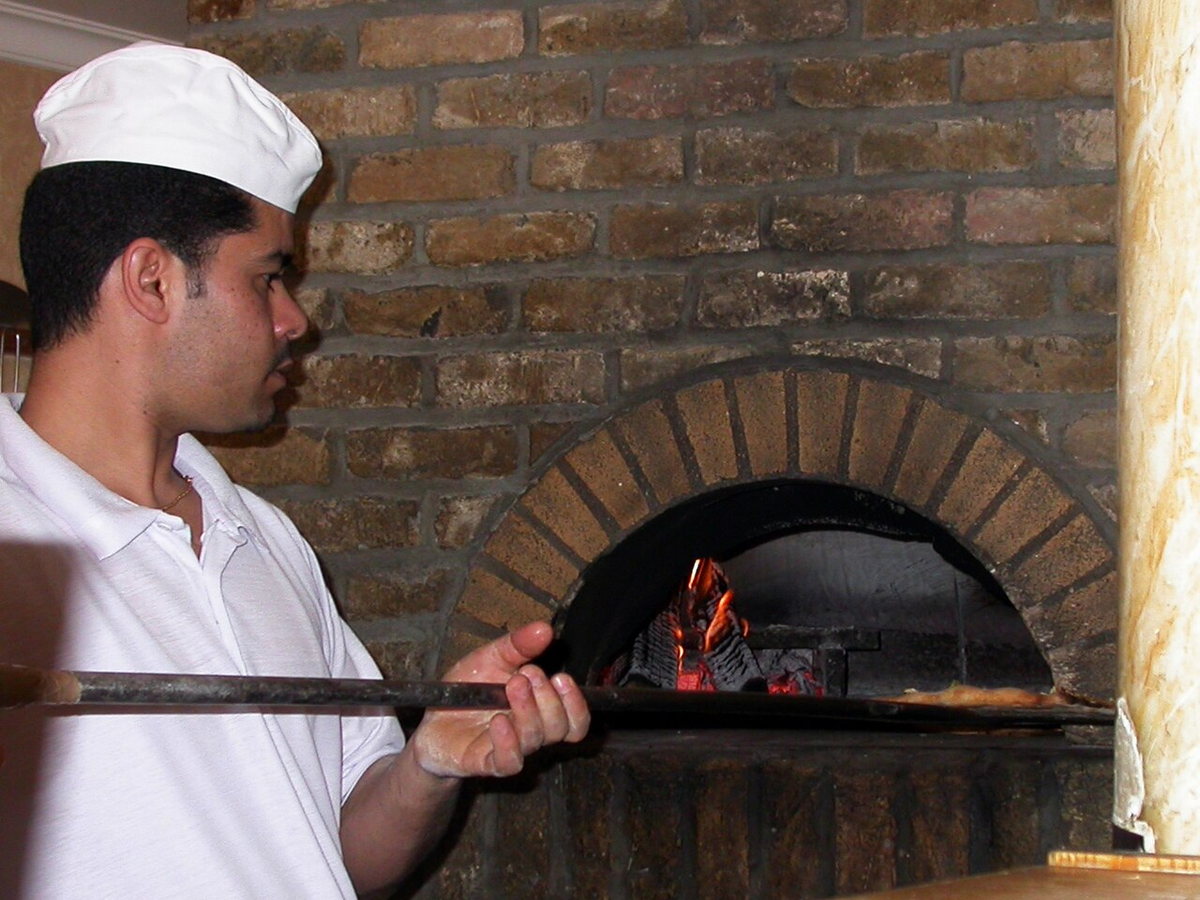Pizza baker tending a pizza inside a brick oven
