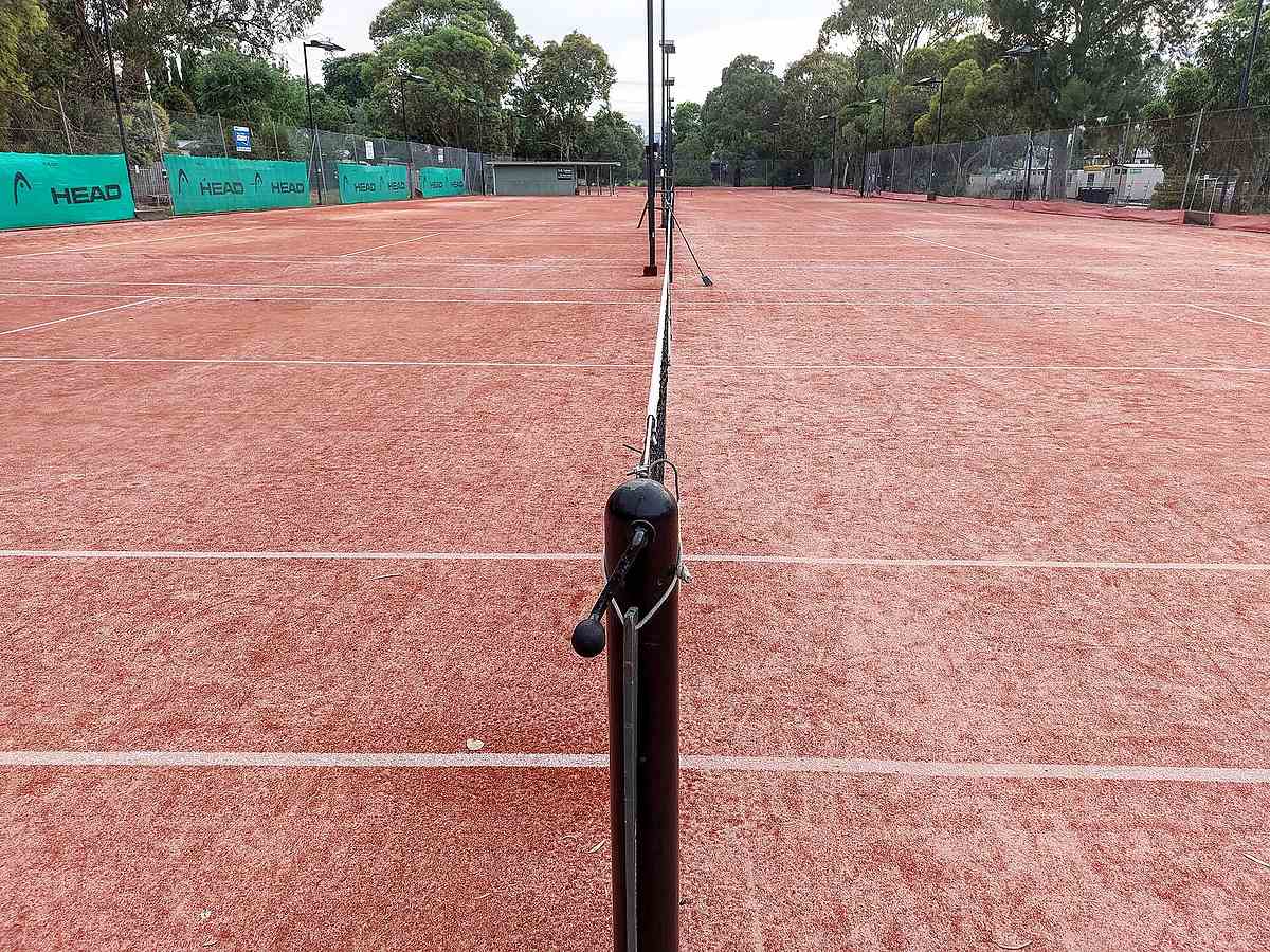 View down the net across a red clay tennis court in Melbourne