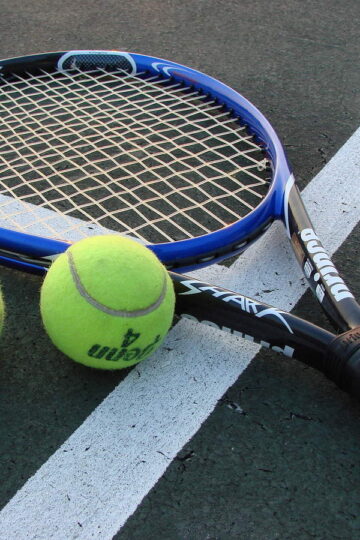 Tennis racket and two yellow tennis balls resting on a hard court