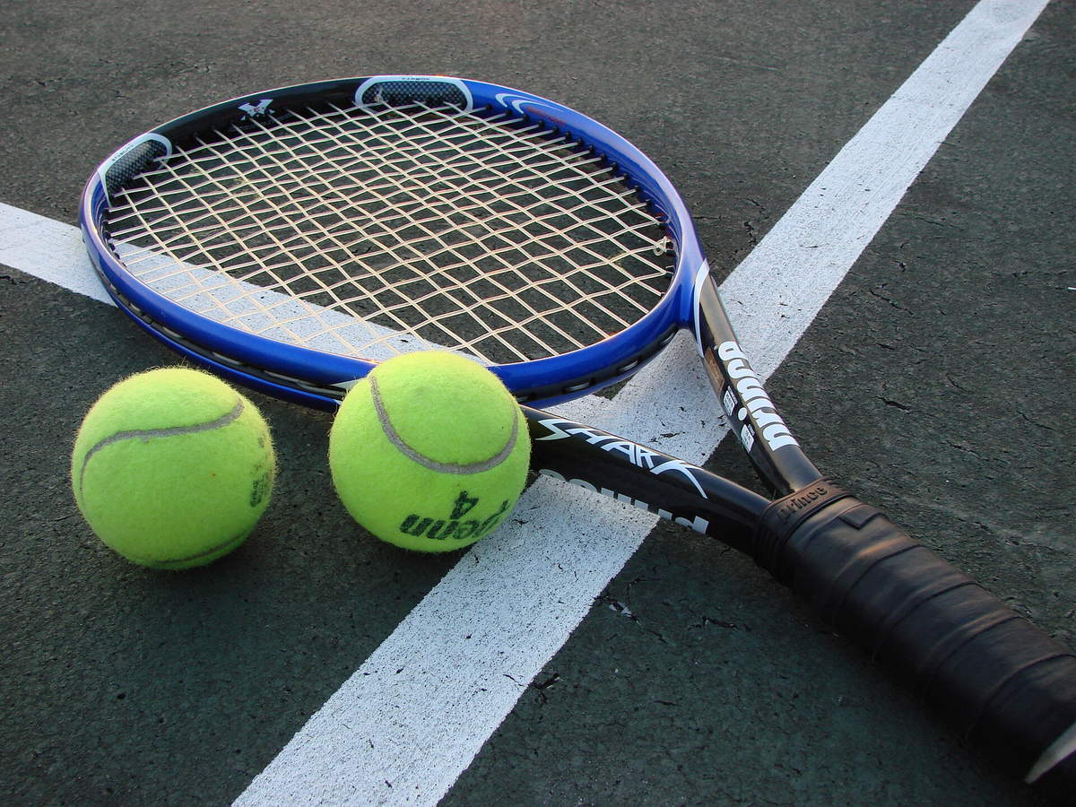Tennis racket and two yellow tennis balls resting on a hard court
