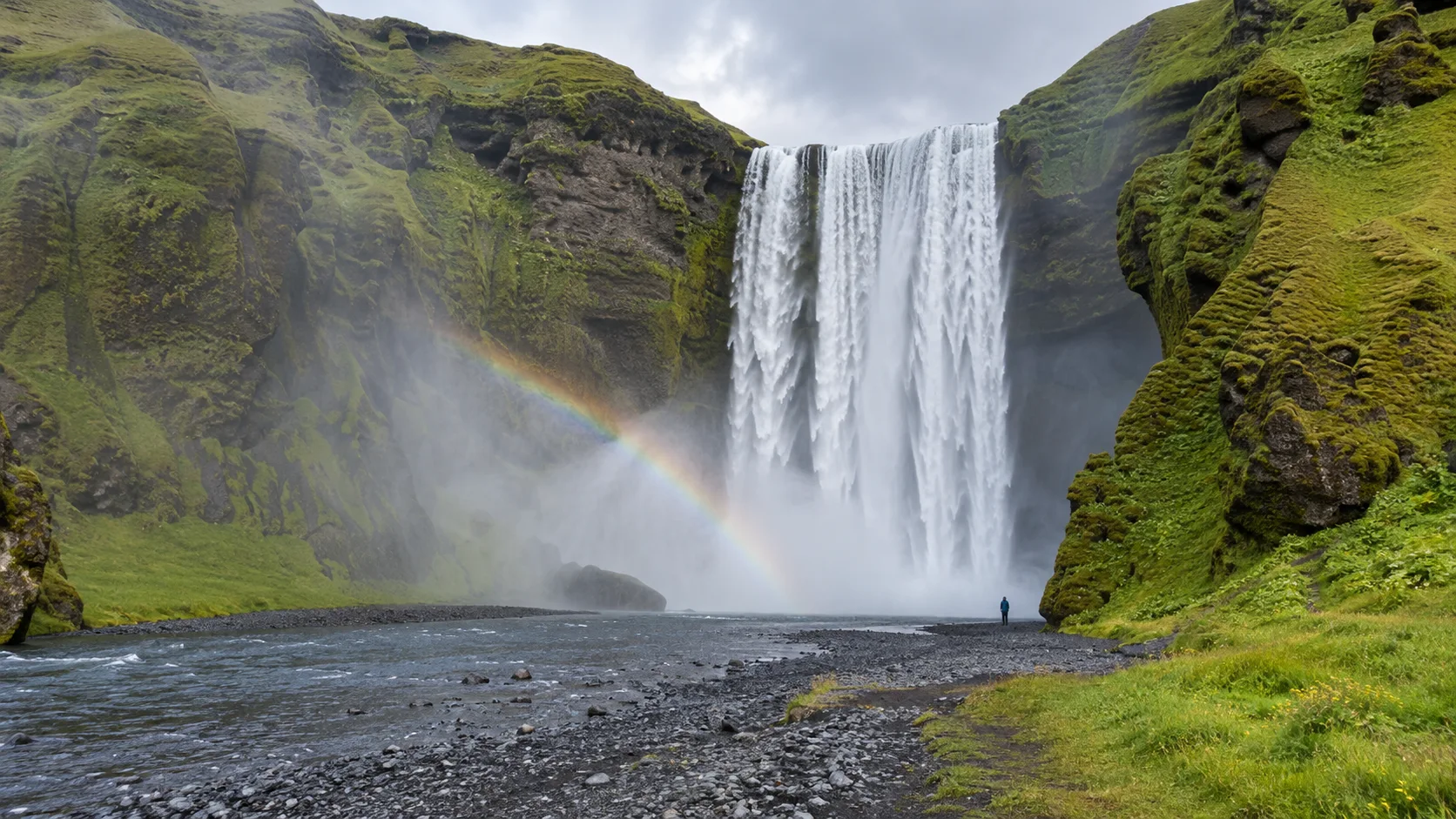 Skógafoss waterfall plunging into mist beneath green Icelandic cliffs