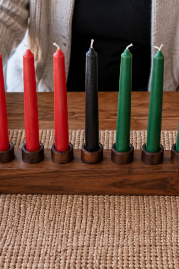 Hands steady a kinara with seven unlit Kwanzaa candles.