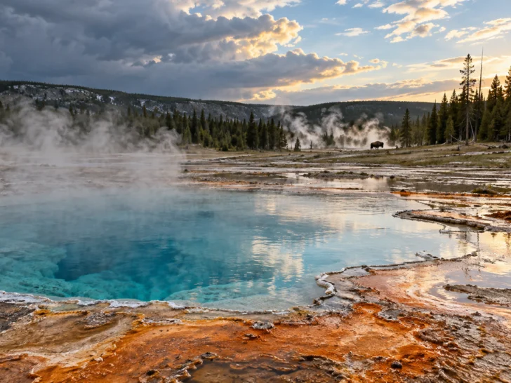 Turquoise hot spring steaming beneath clearing storm clouds