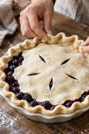 Hands crimping the crust of an unbaked berry pie