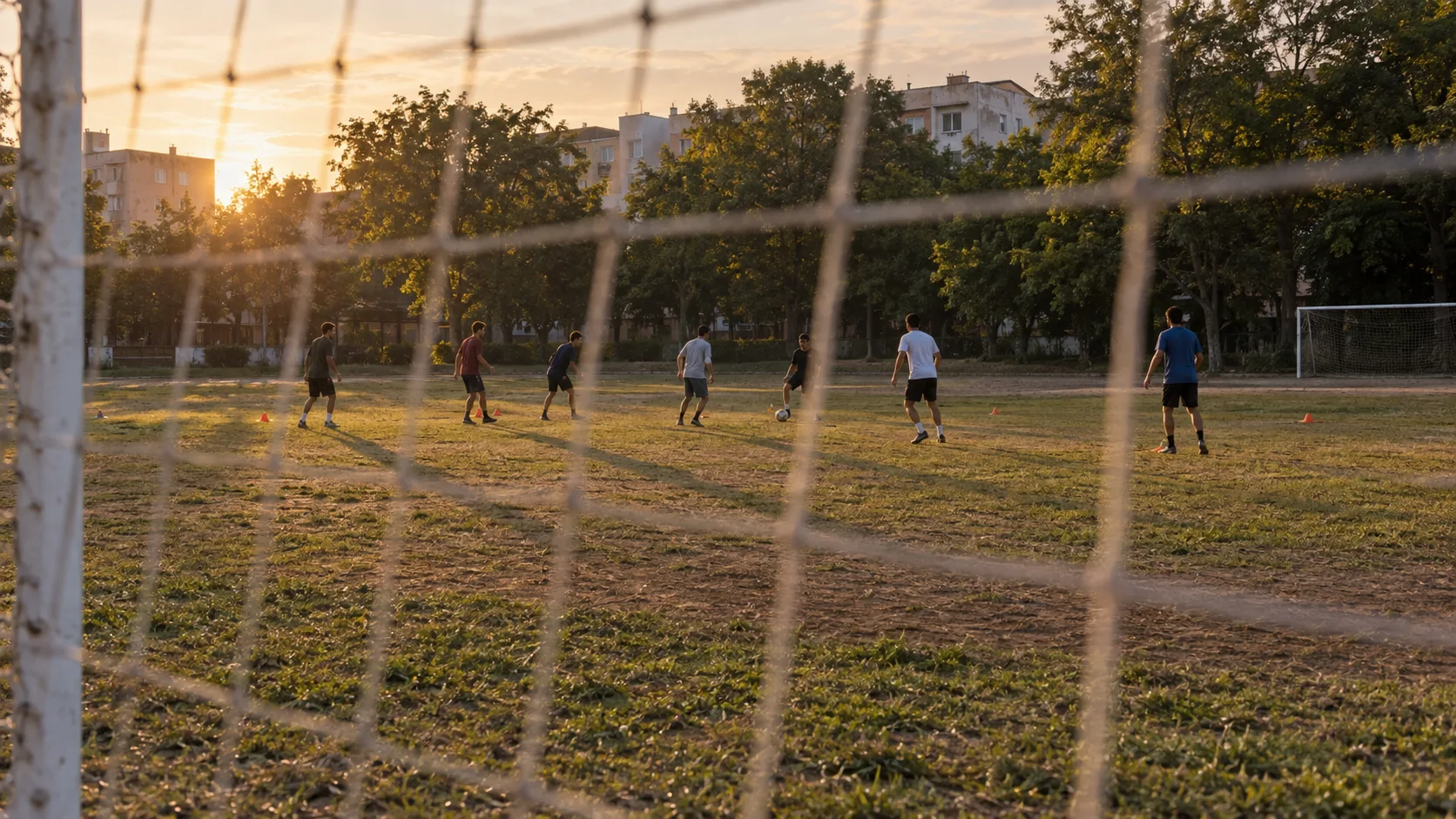 Distant players practice on a neighborhood soccer field at golden hour.