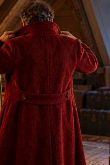 An anonymous adult fits a handmade crimson winter coat in a warm attic.