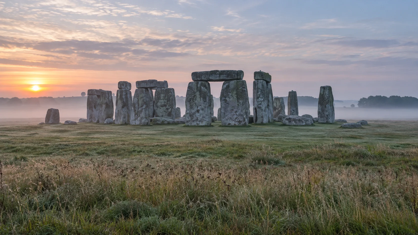 Stonehenge rising from misty grassland at dawn